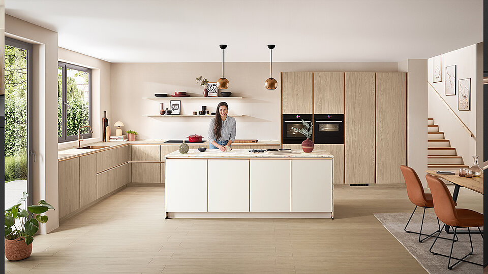 Eine Frau steht in einer Küche neben einem Tisch mit Stühlen.