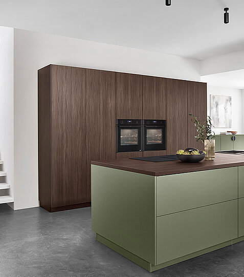 Zeitgemäße Küche mit grünen Küchenschränken und warmen Holzböden, die eine harmonische Atmosphäre erzeugen.